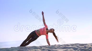 健康，年轻的美女做斜腹压肌练习，在海滩上，日出时，做